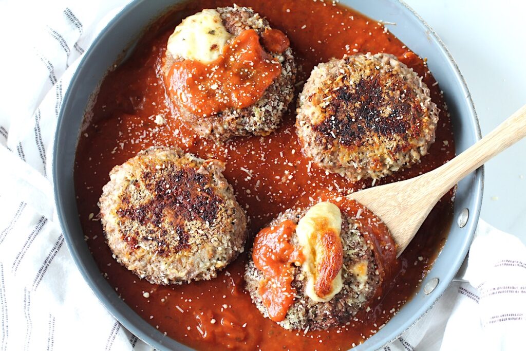 Four Ground beef Polpettone sitting in tomato sauce in a skillet with mozzarella cheese oozing out of a couple of them.