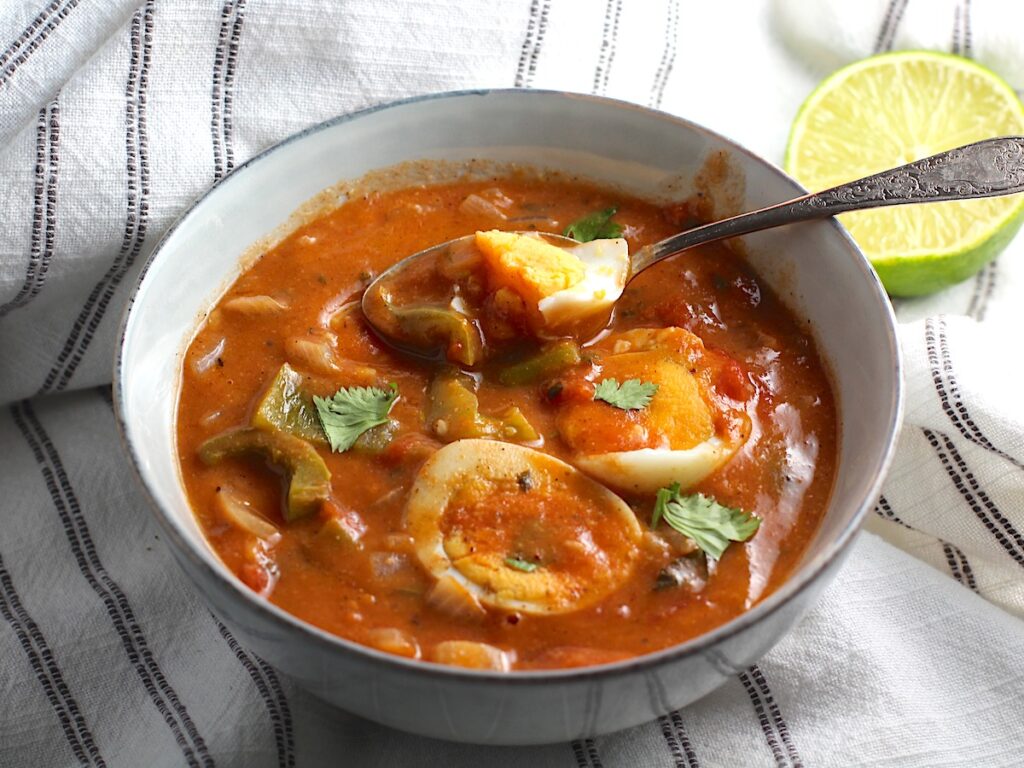 Moqueca de Ovos in a bowl with spoon and sliced hard boiled eggs sitting on top. This is a vegetarian version of a traditional stew in Brazil, where hard boiled eggs replace the seafood.
