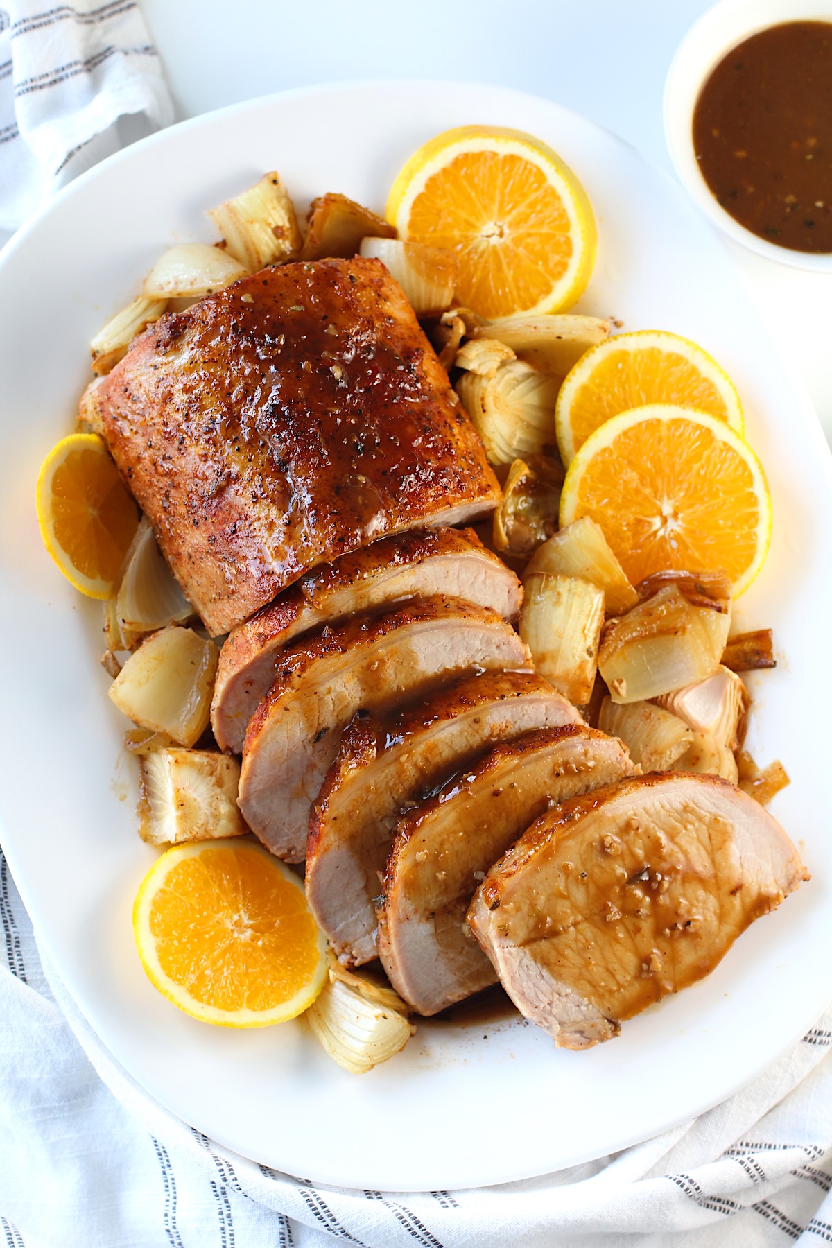 Pork Ribeye Roast Sliced on a platter with Orange Sauce poured over top and onions and orange slices around it.