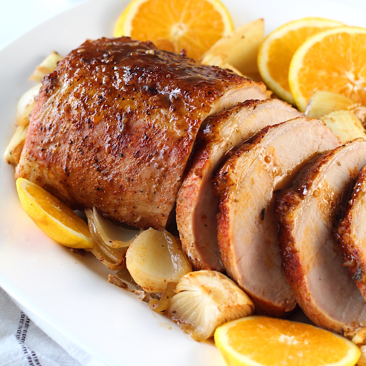 Pork Ribeye Roast Sliced on a platter with Orange Sauce poured over top and onions and orange slices around it.