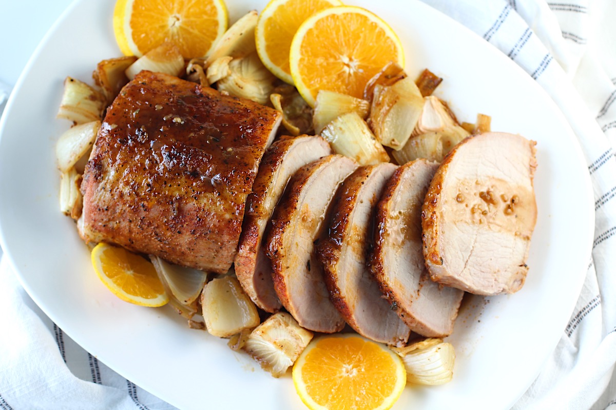 Pork Ribeye Roast Sliced on a platter with Orange Sauce poured over top and onions and orange slices around it.