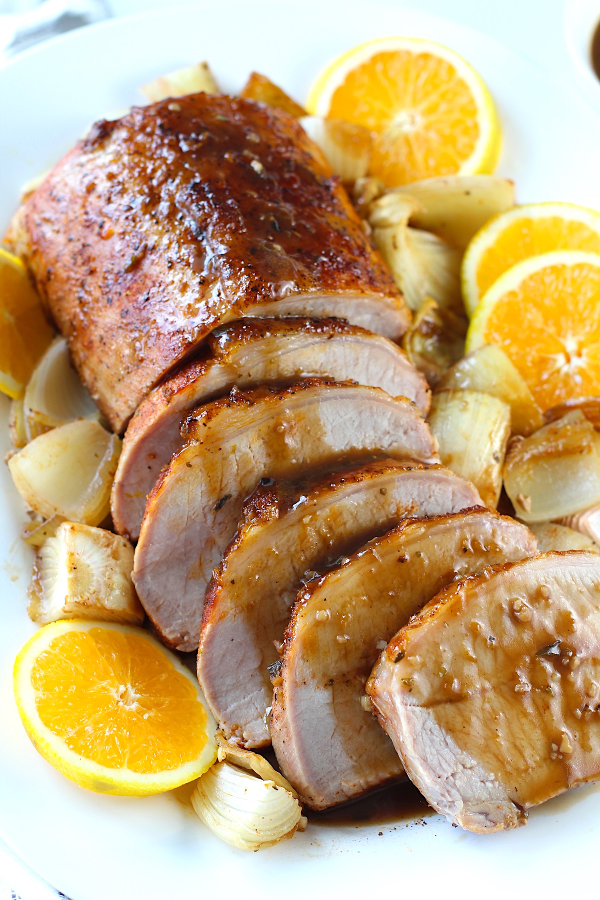 Pork Ribeye Roast Sliced on a platter with Orange Sauce poured over top and onions and orange slices around it.