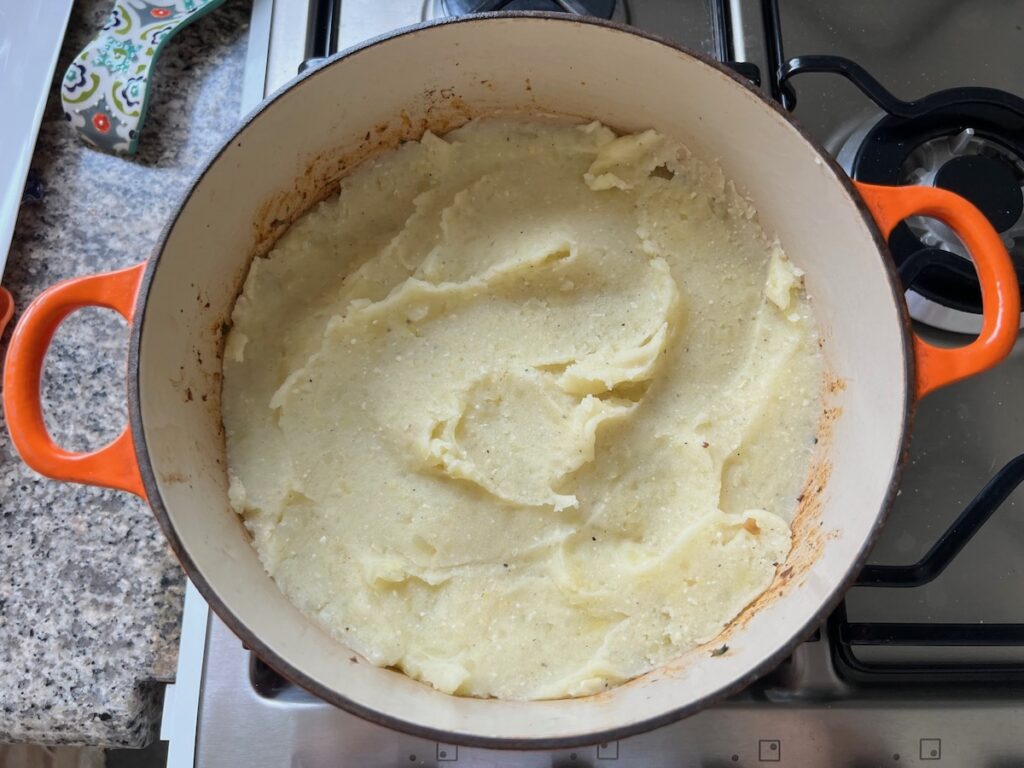 Mashed potatoes spread on top of ground beef filling in a dutch oven on stove for Dutch oven Shepherd's Pie.