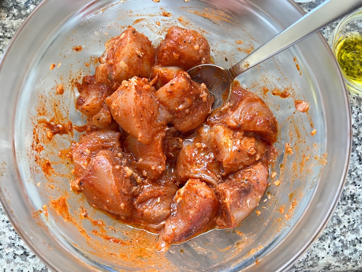 Raw chicken mixed with paprika and garlic and other marinade ingredients for Galinhada, Dutch Oven Chicken and Rice.