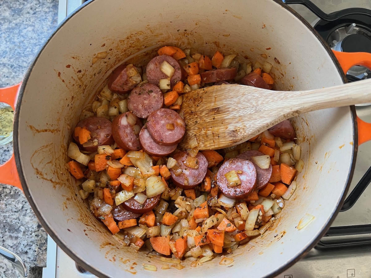 Cooked sausage slices added to Carrots, onions, and garlic cooking in a pot for Galinhada, Dutch Oven Chicken and Rice.