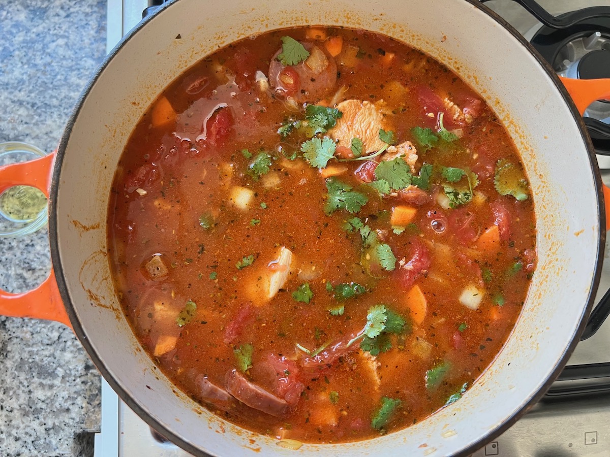 Fresh cilantro leaves added to tomatoes, broth, and chicken in pot for Galinhada, Dutch Oven Chicken and Rice.