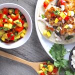 Spicy Mango Salsa in a bowl with a bamboo spoon laying down with a scoop of the salsa and shrimp taco on a plate with the mango salsa on top.