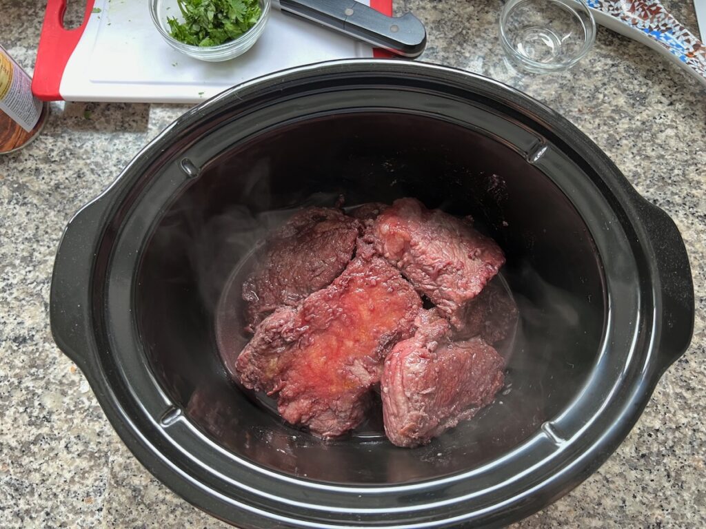 Seared beef ribs and wine in slow cooker pot for Brazilian Vaca Atolada Beef Rib Stew.