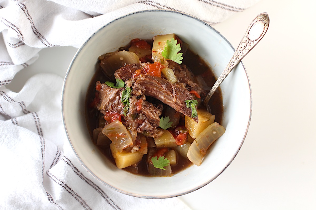 Brazilian Vaca Atolada Beef Rib Stew in a bowl with fork with yucca, onions, garlic, tomatoes, cilantro in a delicious thick beef wine sauce.