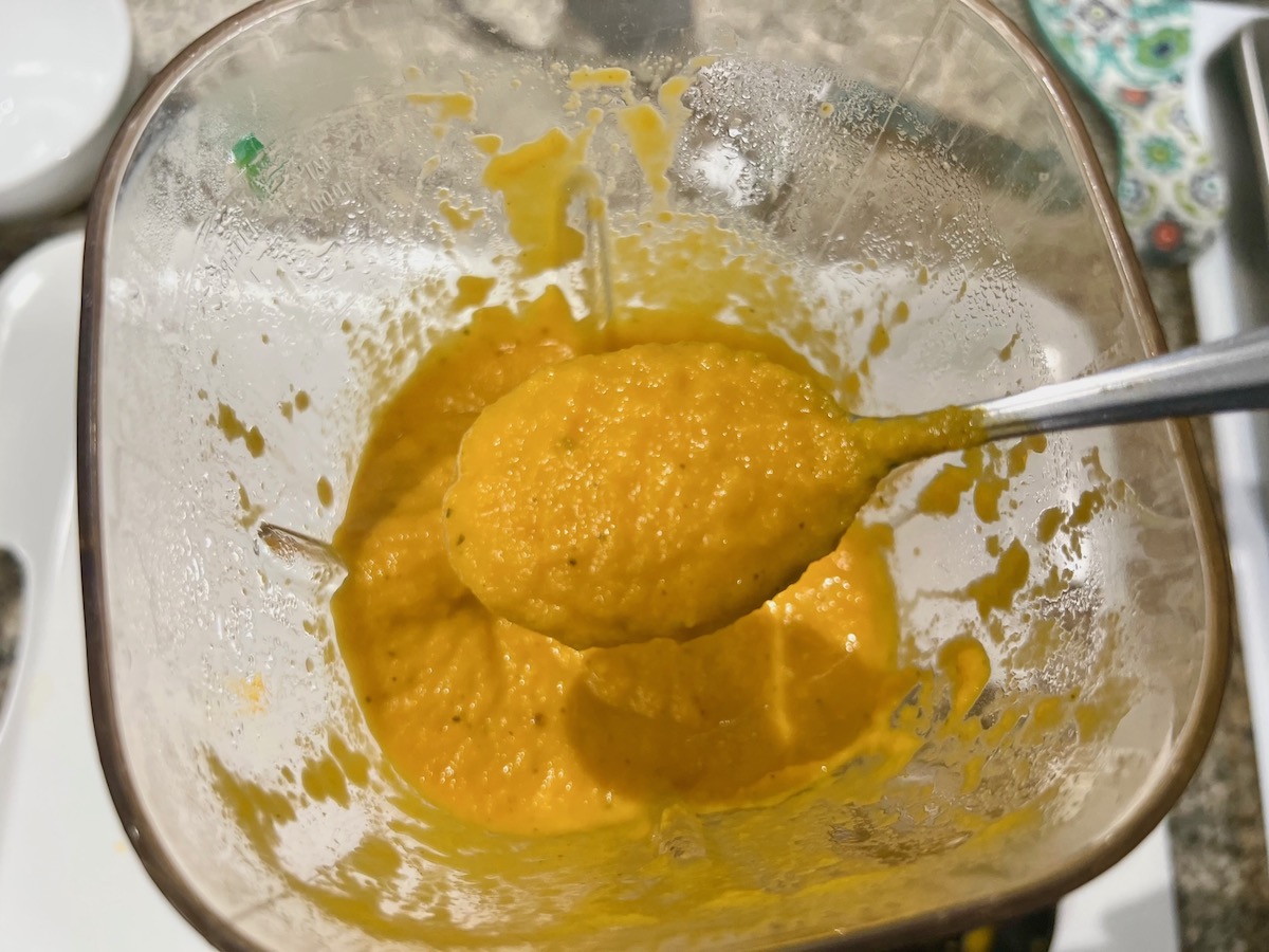 Smooth, blended carrot sauce in a blender with a spoon holding a spoonful over.