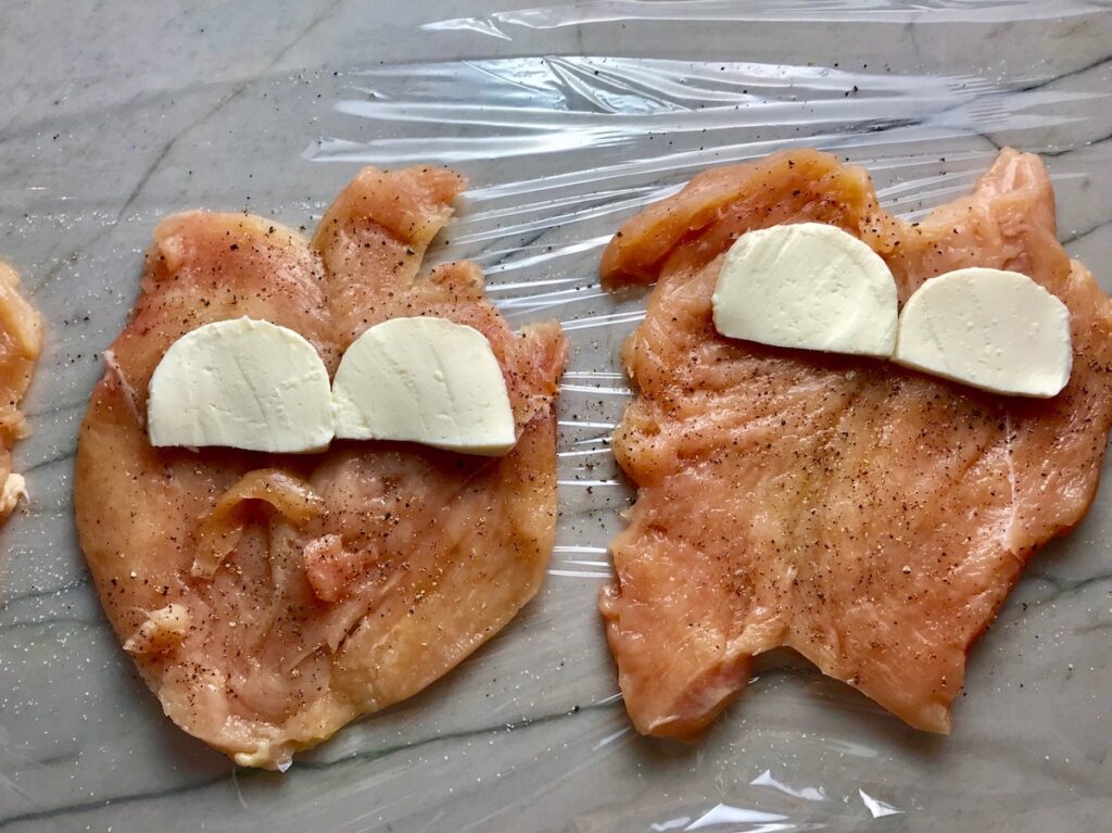 Butterflied and pounded flat chicken breasts seasoned with salt and pepper with slices of mozzarella cheese on top for Mozzarella Stuffed chicken.