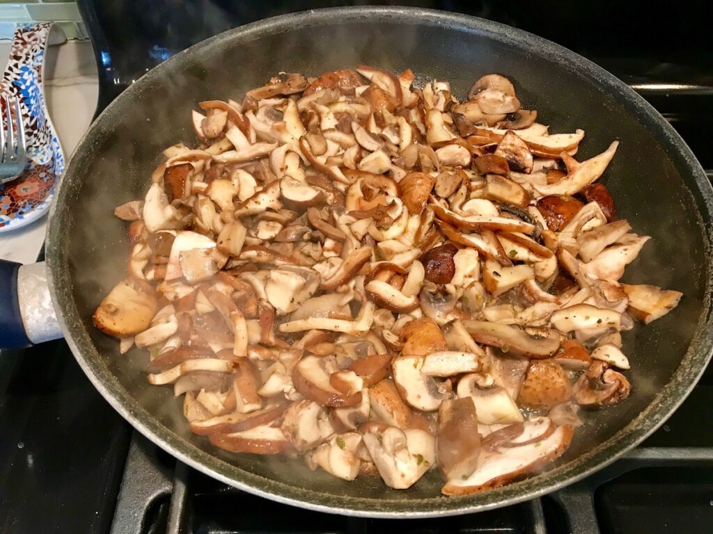 Sliced shiitake and cremini mushrooms cooking in a large skillet on the stove for Mozzarella Stuffed Chicken.