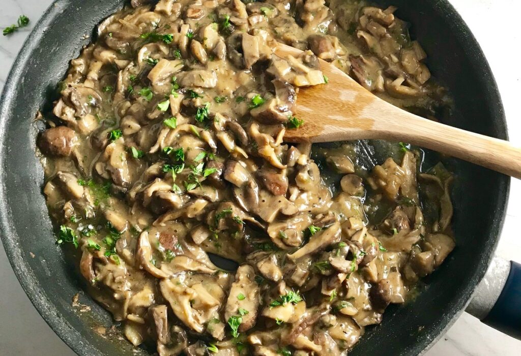Thick and creamy mushroom sauce cooked in a skillet with wood spoon in it and parsley sprinkled on top for Mozzarella Stuffed Chicken rolls.