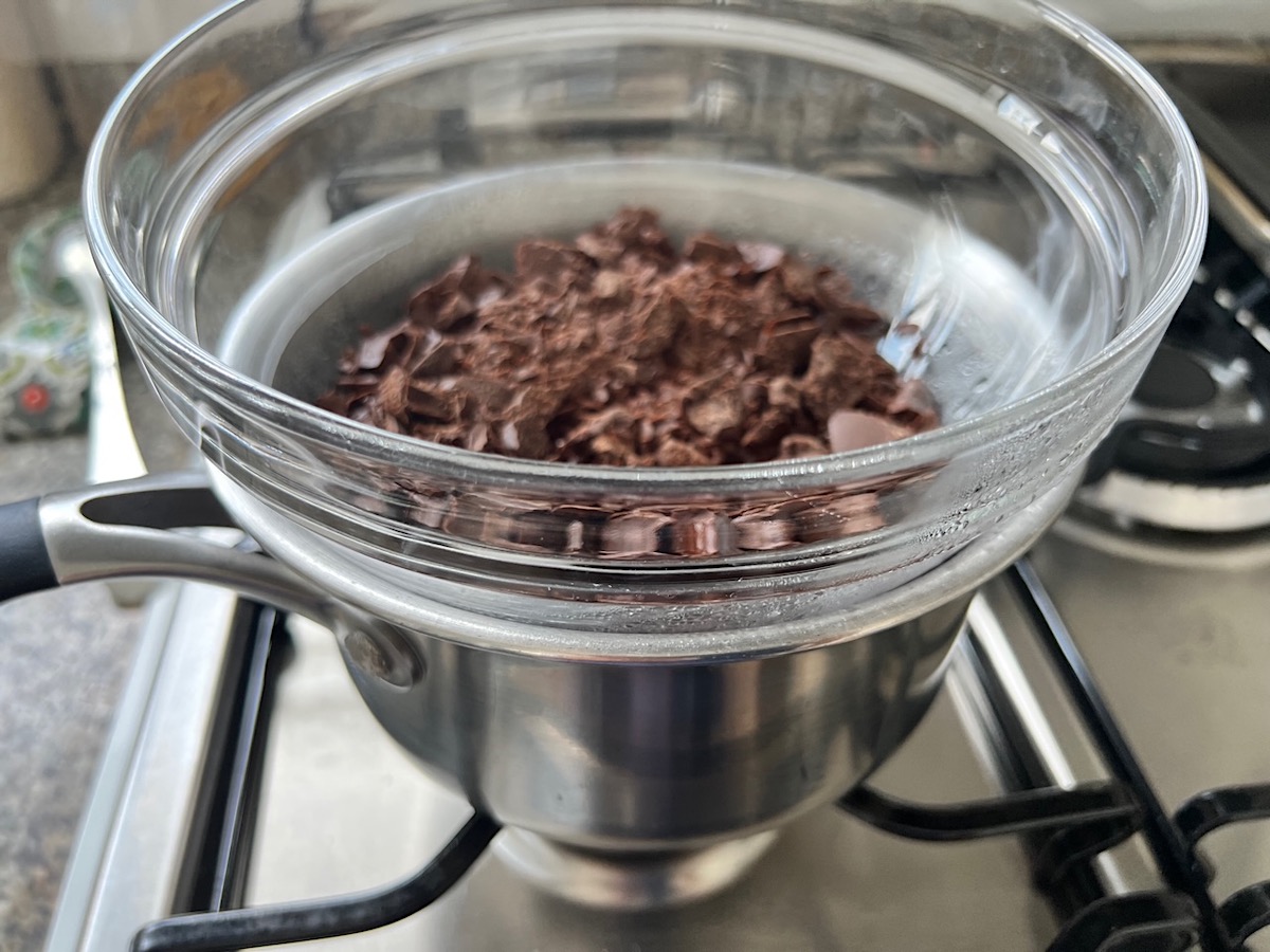 Chocolate pieces in a clear glass bowl sitting on a smaller pot of water on the stove for Brigadeiro Brazilian Cake.