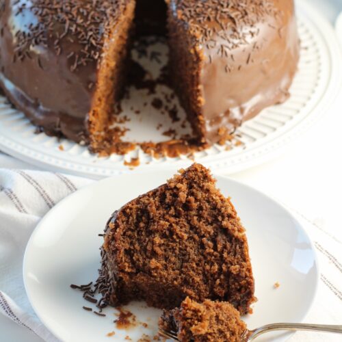 Brigadeiro Brazilian Cake slice on a plate with a fork holding a bite and the rest of the cake in the background on a platter.