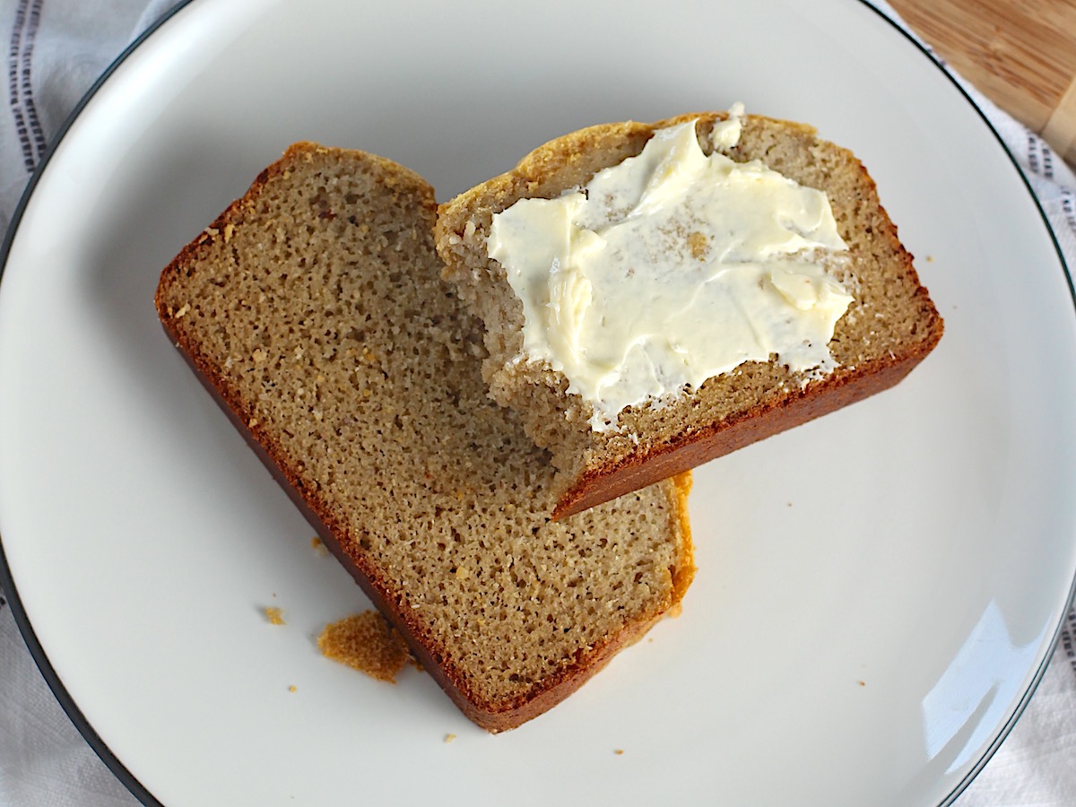 Two slices of Cassava Bread on a plate with the top slice buttered with bites taken out..