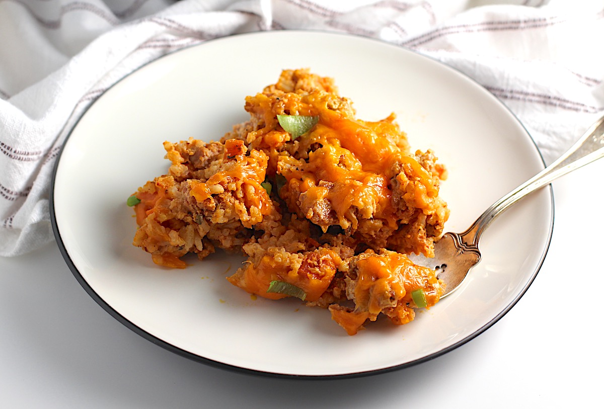 Plate on counter with Ground Pork Slow Cooker Casserole on it and melted cheese on top. A fork is on plate with a bite of the casserole scooped.