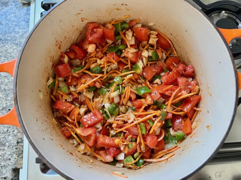 Tomatoes, green peppers, onions, and carrots cooking in a pot for Summer Beef Stew Picadinho.