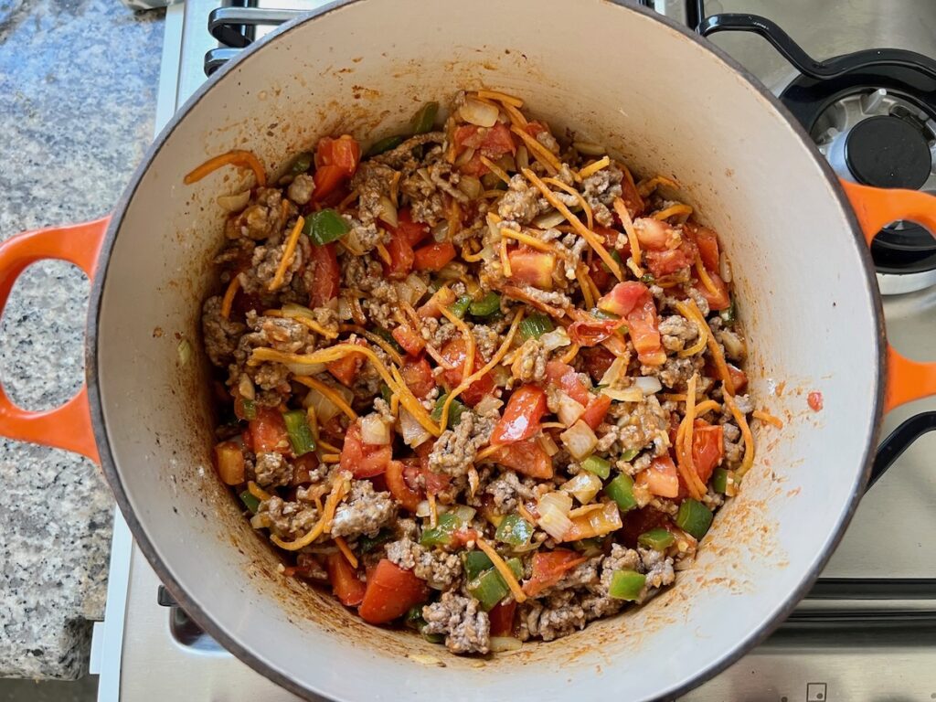 Ground beef, tomatoes, green peppers, onions, and carrots cooking in a pot for Summer Beef Stew Picadinho.