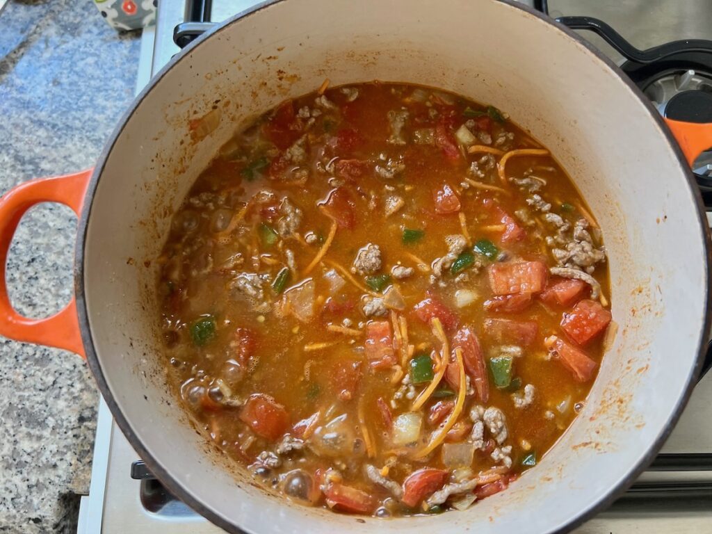 Broth, Ground Meat, tomatoes, green peppers, onions, and carrots cooking in a pot before being reduced for Summer Beef Stew Picadinho.