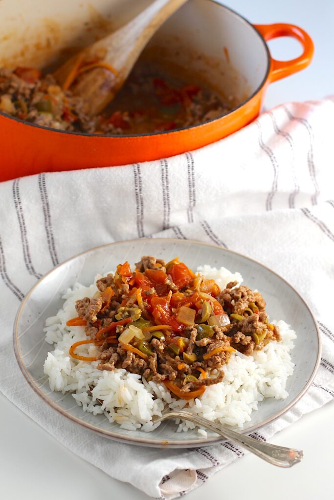Summer beef stew over rice on a plate with pot in background on counter. It's based on Brazilian Picadinho.