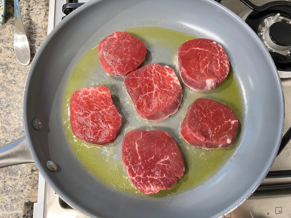 Six beef filet medallions in a pan starting to cook for Beef and Garlic Sauce recipe.