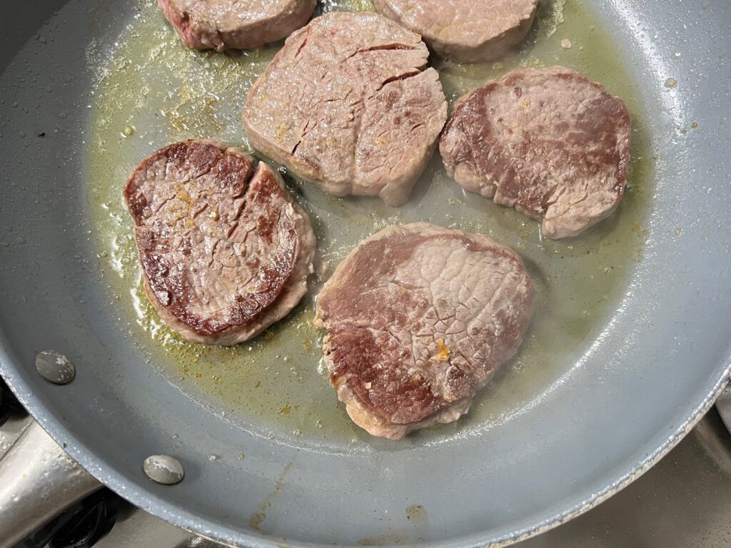 Six beef filet medallions cooked in a pan starting to cook for Beef and Garlic Sauce recipe.