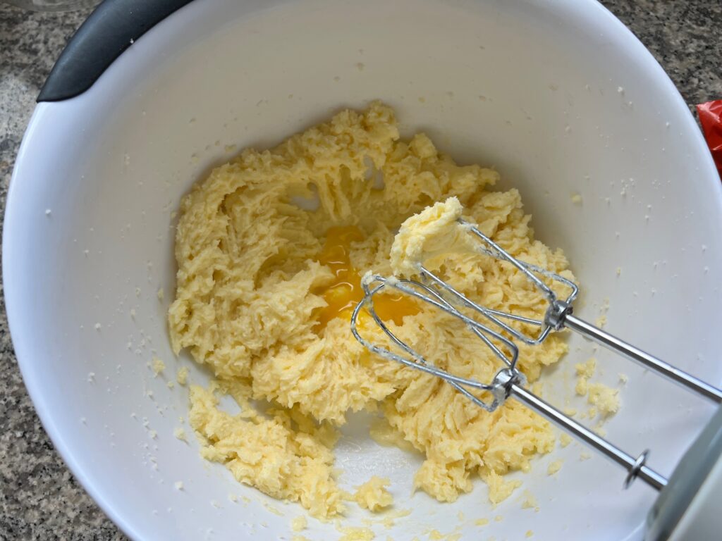 Hand mixer mixing an egg into creamed butter and sugar in a bowl for Cake with Lime recipe.