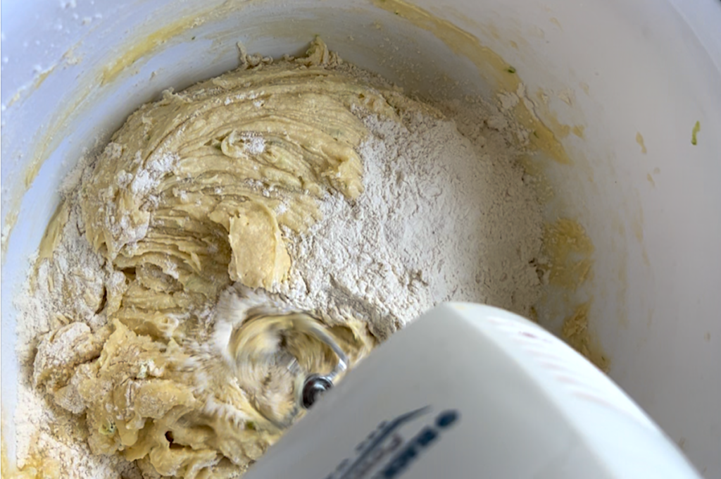 Hand mixer mixing flour into batter in a bowl for Cake with Lime recipe.