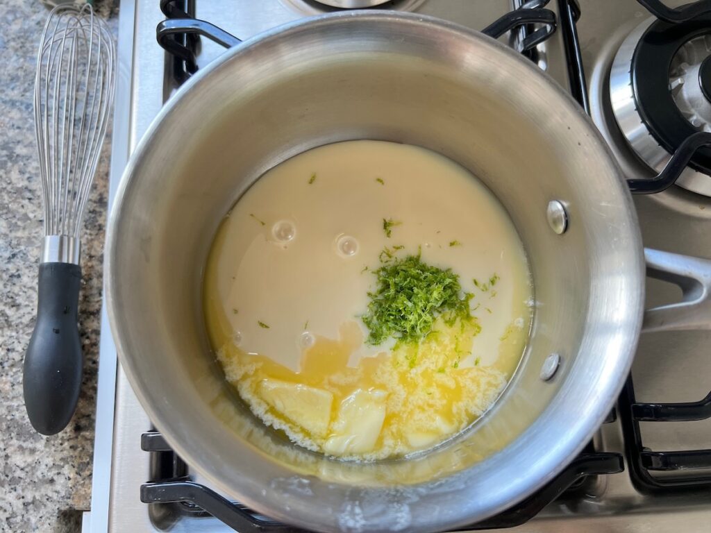 Sweetened condensed milk, lime juice, lime zest, and butter melting in a saucepan for Cake with Lime recipe.