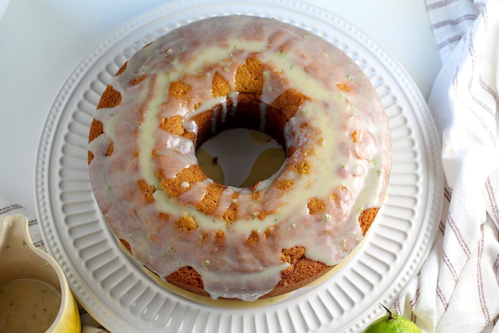 Whole vanilla bundt cake with lime on a platter with glaze poured over top and dropping on to the platter.