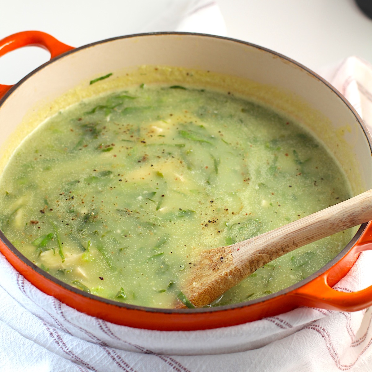 Chicken Kale Soup thickened with pureed potatoes (Caldo Verde com Frango) in a pot with wood spoon on table with towel.