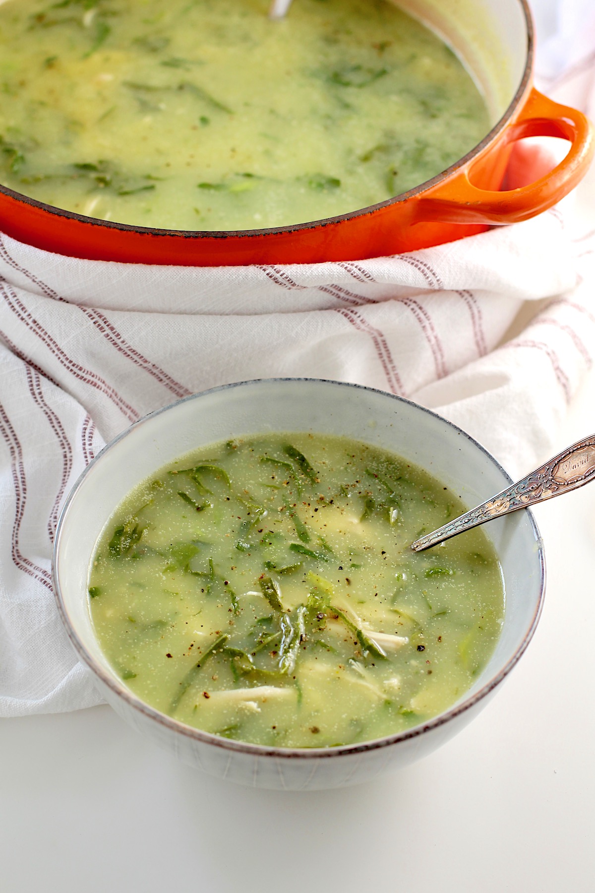 Chicken Kale Soup thickened with pureed potatoes (Caldo Verde com Frango) in a bowl with spoon on table with pot of soup in the background.