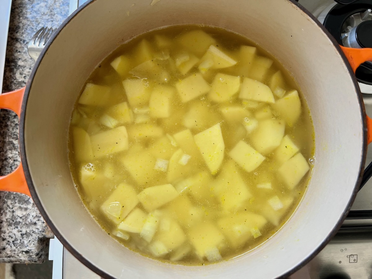 Broth added to potatoes, onions, and minced garlic added to pot on stove for Chicken Kale Soup thickened with pureed potatoes (Caldo Verde com Frango).