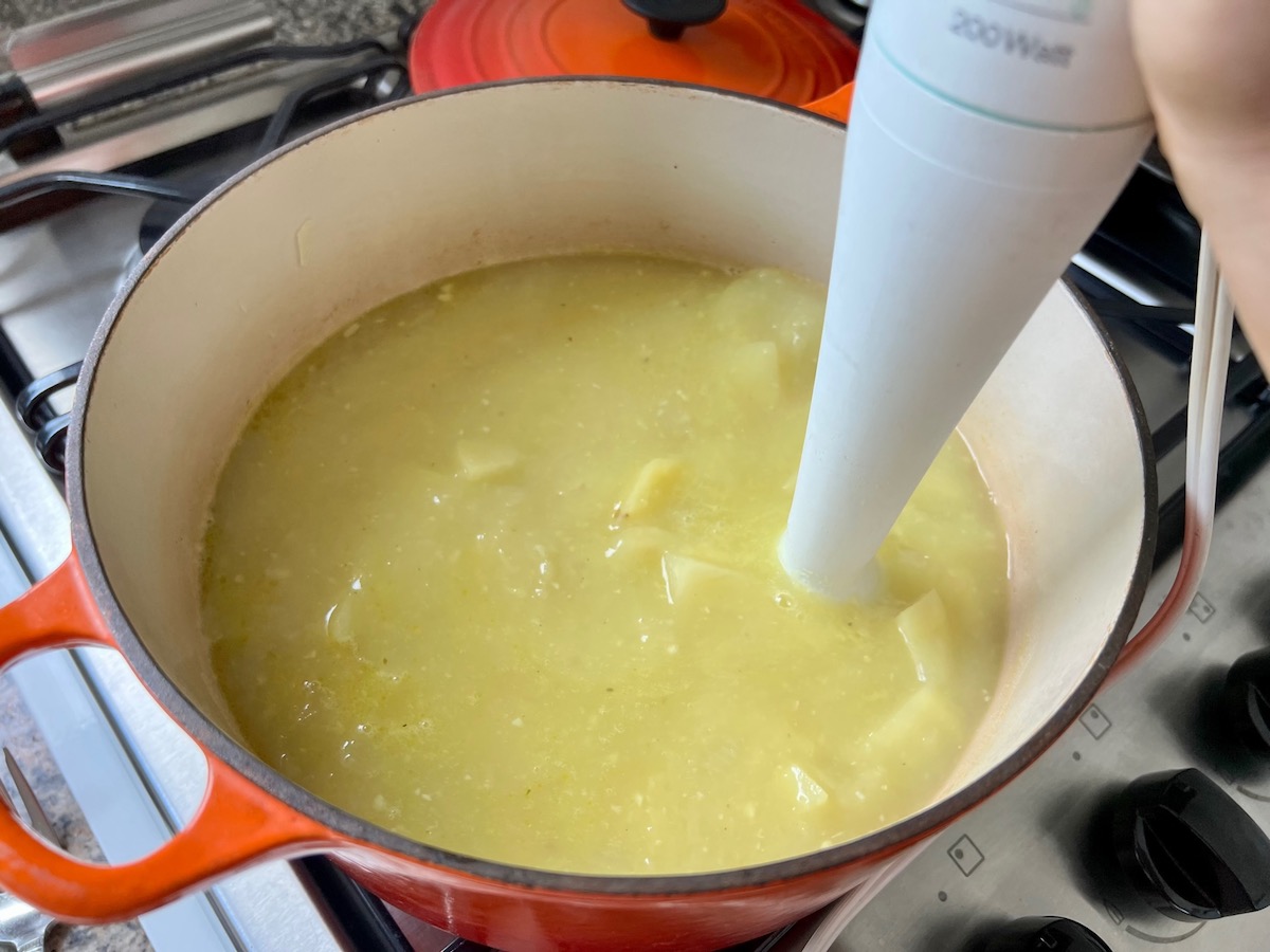 Immersion blender in the pot blending the potatoes for Chicken Kale Soup thickened with pureed potatoes (Caldo Verde com Frango) in a pot on stove.