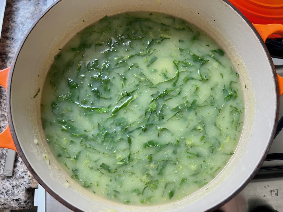 Shredded kale mixed into to pureed potato soup for Chicken Kale Soup thickened with pureed potatoes (Caldo Verde com Frango) in a pot on stove.