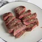 Sliced Filet of beef with garlic sauce on a plate with skillet with more beef in background.