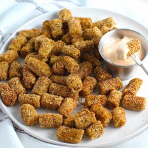Breaded okra cooked in air fryer on a plate with a dipping sauce.