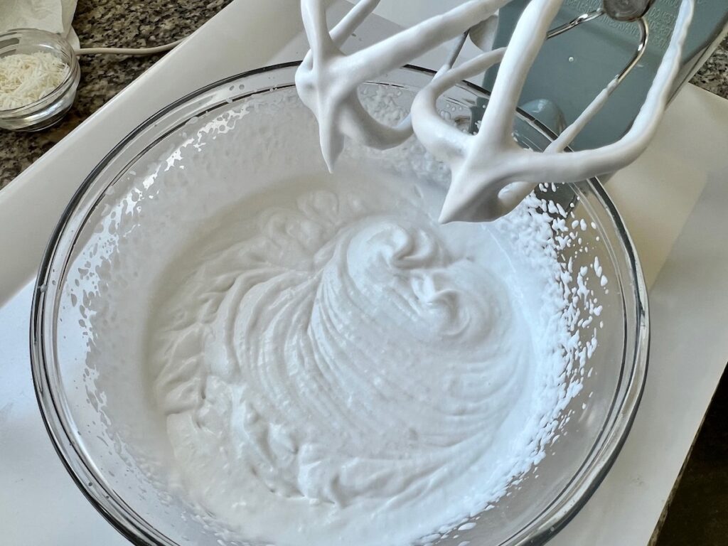 Whipped coconut cream in bowl with hand mixers showing light stiff peaks for Coconut Ice Cream Recipe without Cream.