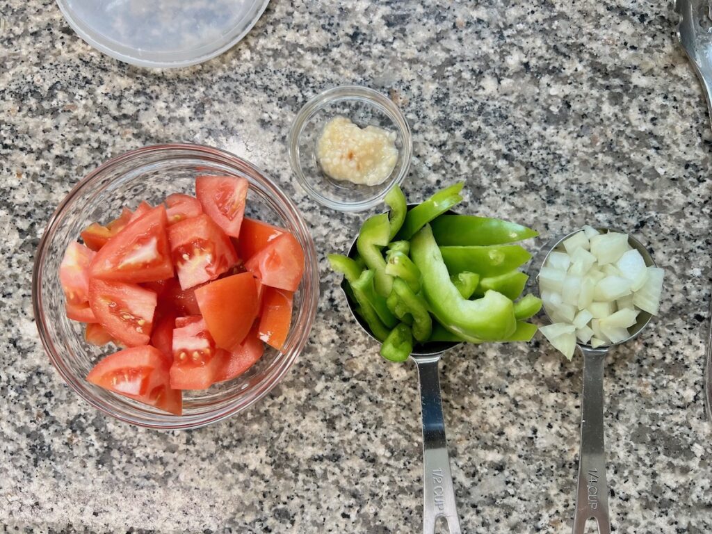 Tomatoes chopped in a bowl, green peppers sliced, onions diced in a measuring cup, and garlic minced for Coconut Milk Pasta Sauce Recipe.