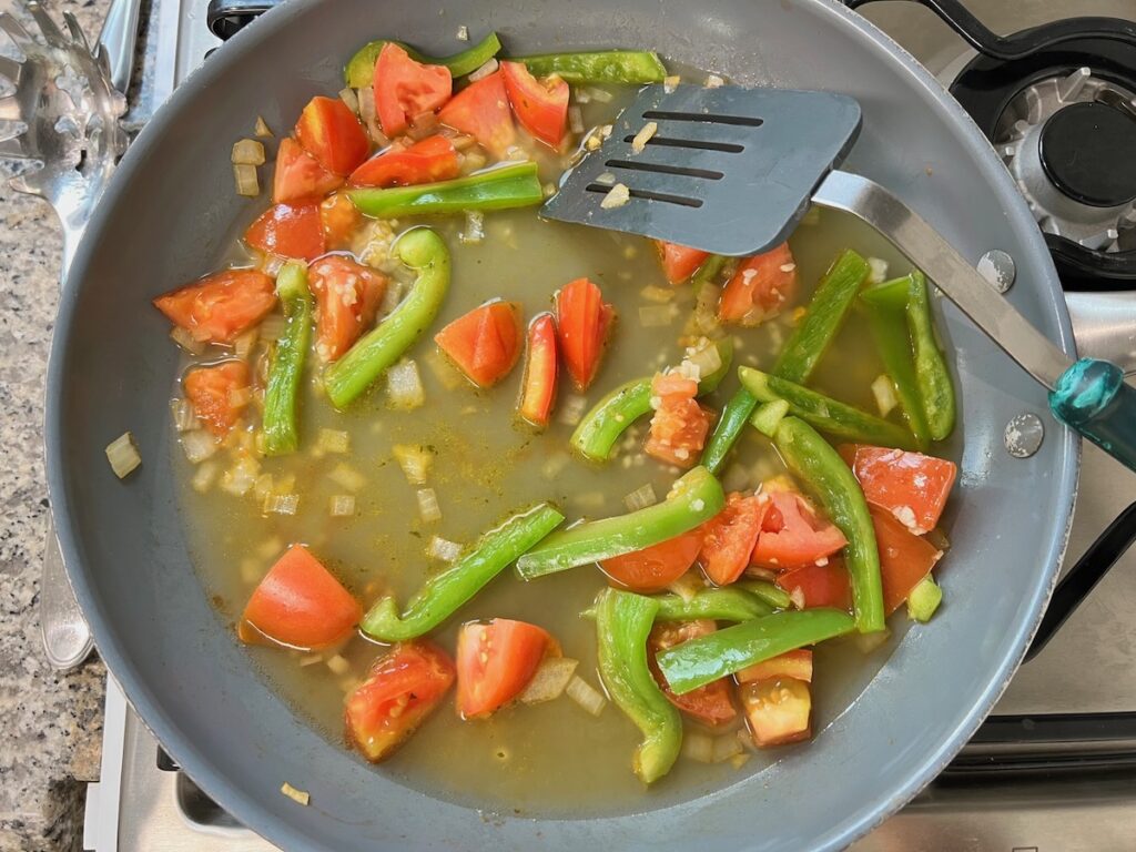Broth and garlic added to onions, green pepper, and tomatoes in pan cooking for Coconut Milk Pasta Sauce.
