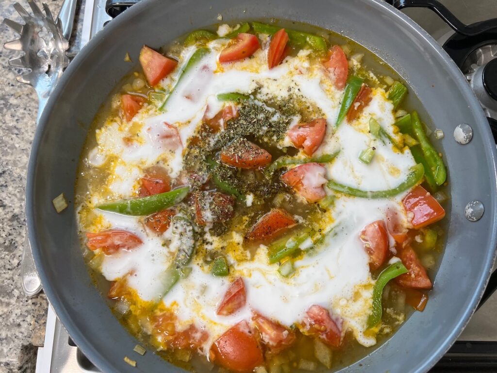 Coconut milk and seasonings added to garlic, onions, green pepper, and tomatoes in pan cooking for Coconut Milk Pasta Sauce.