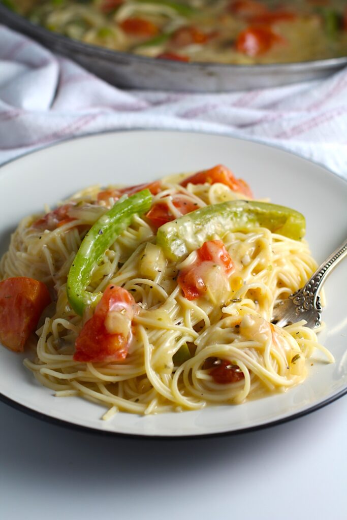 Coconut Milk Pasta Sauce with tomatoes and green pepper mixed with spaghetti pasta on a plate with fork holding a bite of pasta.