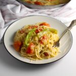 Coconut Milk Pasta Sauce with tomatoes and green pepper mixed with spaghetti pasta on a plate with fork holding a bite of pasta.