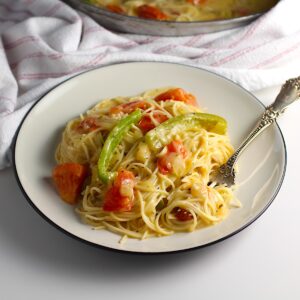 Coconut Milk Pasta Sauce with tomatoes and green pepper mixed with spaghetti pasta on a plate with fork holding a bite of pasta.