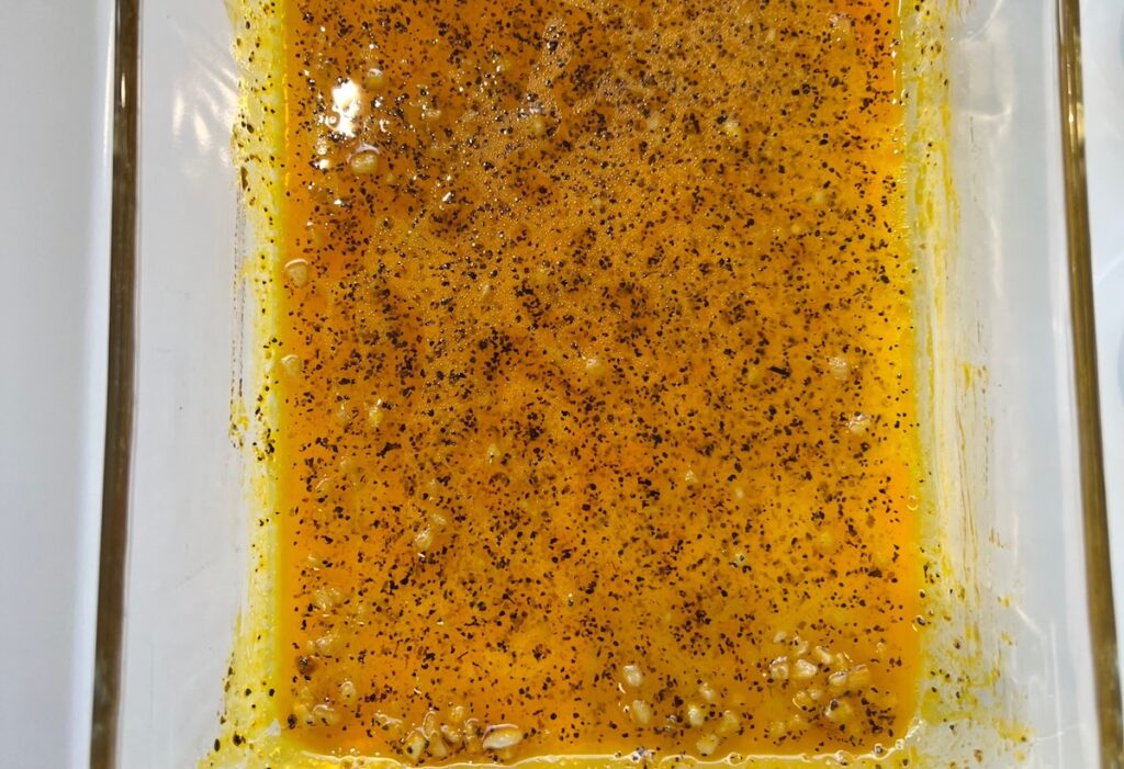 Marinade with honey, garlic, lemon pepper seasoning, olive oil, and water in a glass dish for the Honey Lemon Pepper Chicken recipe.
