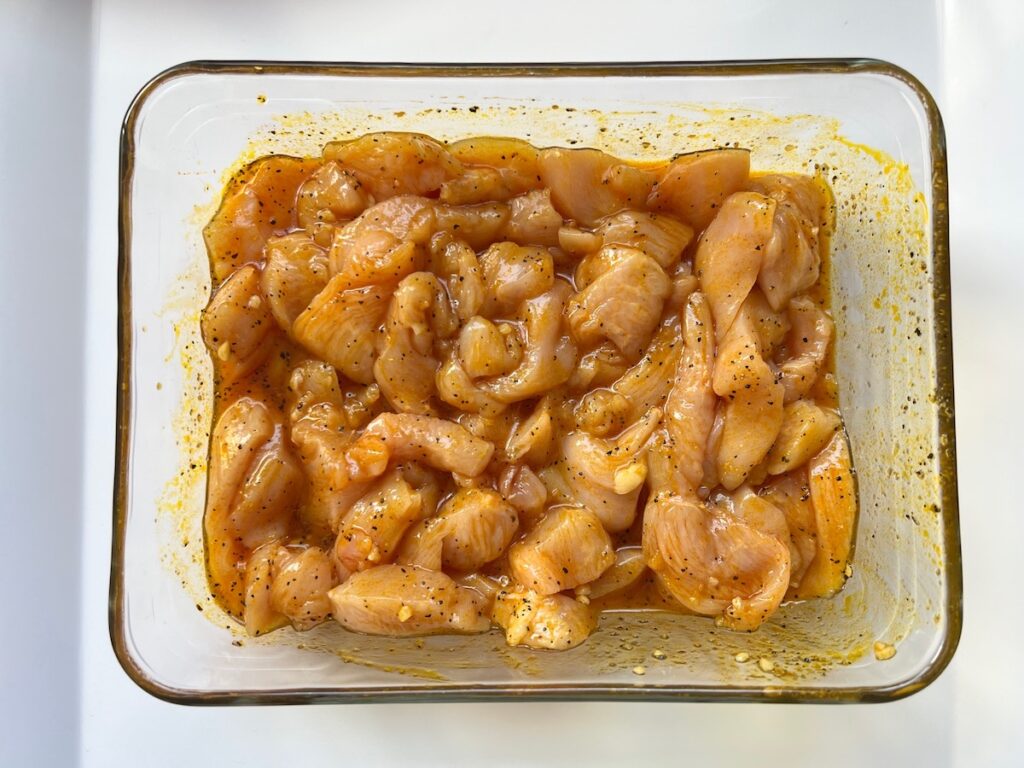 Raw chicken pieces in marinade with honey, garlic, lemon pepper seasoning, olive oil, and water in a glass dish for the Honey Lemon Pepper Chicken recipe.