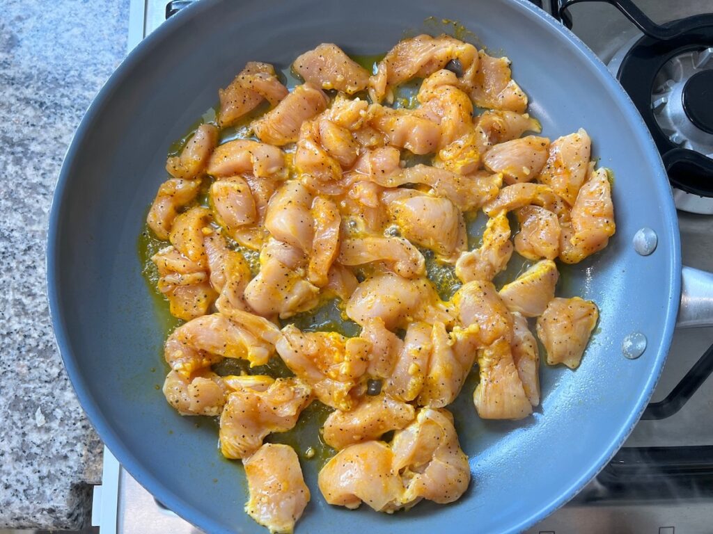 Raw marinated chicken pieces in a skillet starting to cook on stove for Honey Lemon Pepper Chicken recipe.