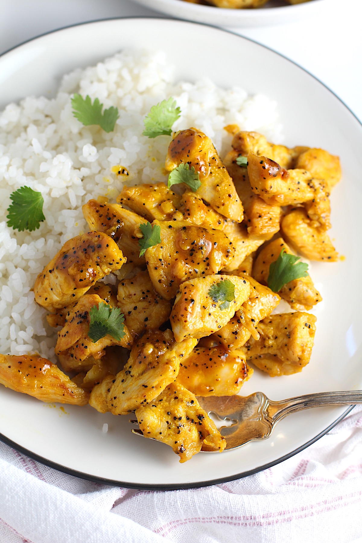 Honey Lemon Pepper Chicken bites over white rice with fresh cilantro leaves on top.