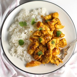 Honey Lemon Pepper Chicken bites over white rice with fresh cilantro leaves on top.